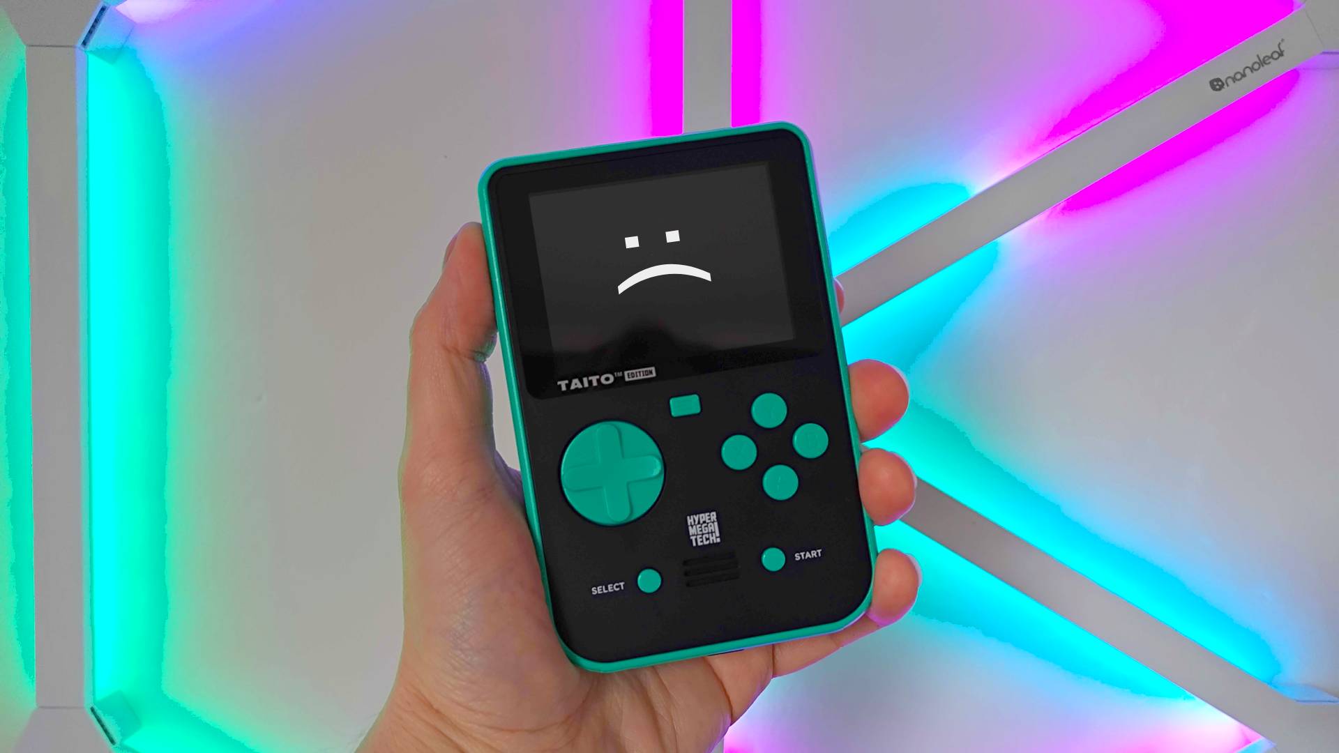 Green and Black Taito Super Pocket handheld with RGB lights in backdrop and sad text face on screen