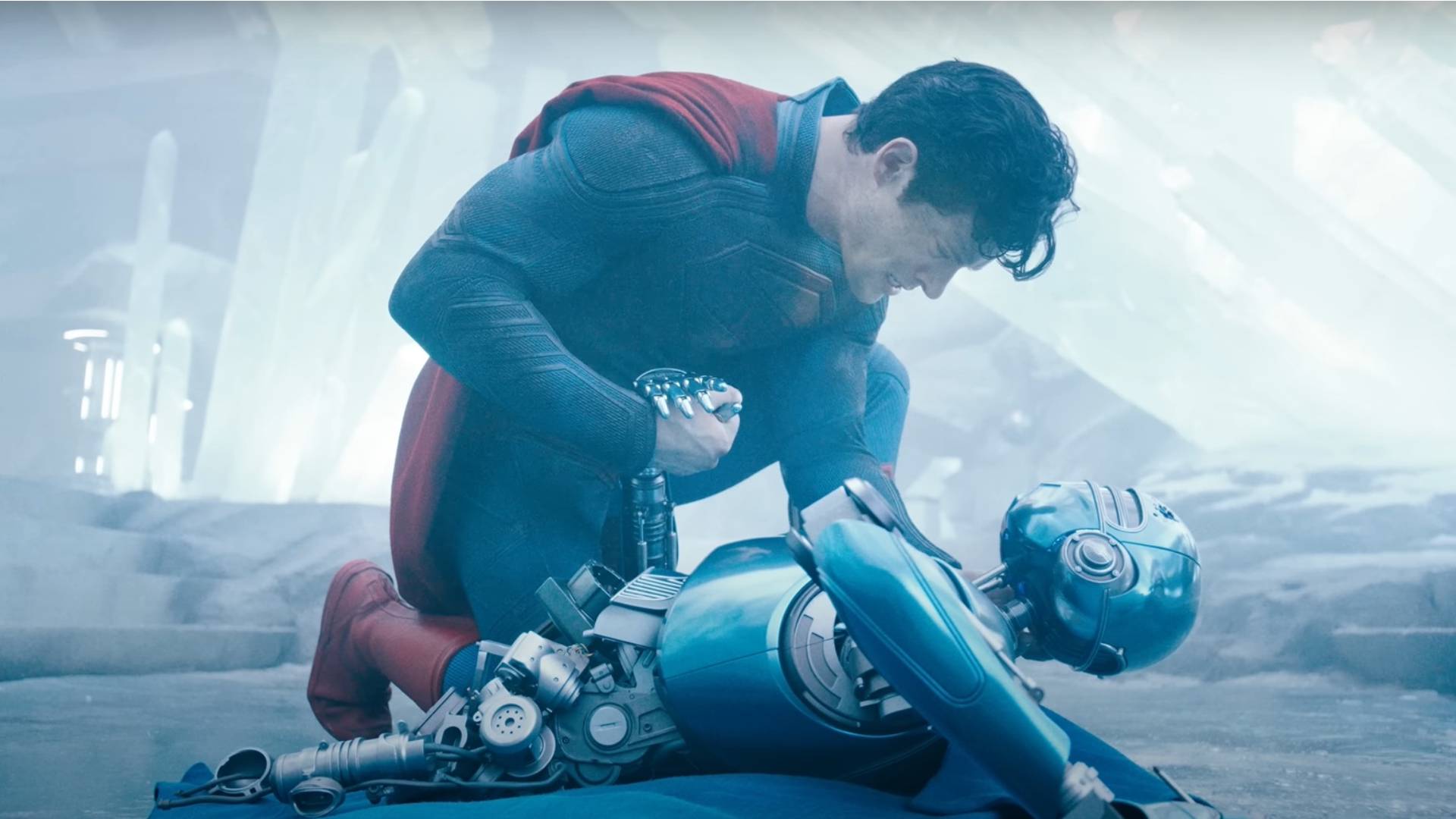 David Corenswet as Superman kneels by a broken robot in the new Superman movie.
